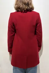 Tapado de paño de lana color gris, con solapas clásicas, cierre frontal de dos botones, bolsillos laterales con solapa y un bolsillo superior en el pecho. Presenta un tajo en la parte posterior y forro interior.