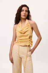 Top amarillo con cuello halter, frunces y jaretas ajustables en el frente. Espalda descubierta. Confeccionado en lino y algodón.
