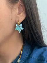 Aro tipo argolla de acero quirúrgico con dije en forma de estrella de color celeste, decorado con cristales brillantes aplicados a mano.