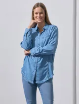 Camisa celeste de tencel, marca Hester & Orchand. Tiene cuello con solapa, escote en V, abertura central con botones, bolsillo aplicado en el frente y ruedo desflecado.