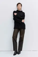 Sweater de punto con diseño de trenzas, cuello alto y mangas largas con puños acampanados. Presenta un corte holgado con terminación asimétrica en el ruedo.