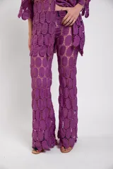 Pantalón de corte evasé color violeta, confeccionado en tela calada de círculos de algodón, con elástico y cierre en la cintura.