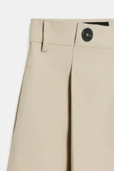 Short de tiro alto color marrón, con pliegues frontales y detalle de botones decorativos en la cintura. Cuenta con bolsillos laterales y cierre frontal con cremallera y gancho metálico.