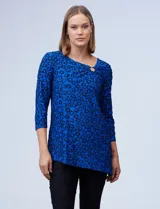 Blusa azul con estampado de círculos negros, de tejido texturado con escote en V descentrado y aplique de aro metálico.