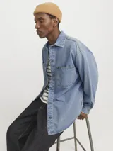 Sobrecamisa de denim celeste, de corte amplio, con cuello clásico, cierre frontal con botones, mangas largas y bolsillos de parche en el pecho.