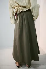 Falda midi tipo capa de tiro medio, confeccionada en mezcla de algodón color verde militar. Cuenta con cintura con trabillas, bolsillos de vivo en los laterales, cierre lateral con cremallera oculta y aplicación de cinturón marrón de estilo western con hebilla metálica grabada.