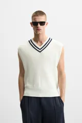 Chaleco de punto color crema con cuello en pico y ribete azul marino. Sin mangas y corte relajado.