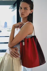 Bolso de hombro formato maxi de piel, en combinación de colores rojo y bordó. Cuenta con detalle de pespuntes, bolsillo interior con cremallera extraíble y cierre mediante fruncido con asas finas de hombro.