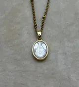 Collar de cadena dorada con eslabones pequeños y detalles de esferas, que sostiene un dije circular con la imagen de la Virgen tallada sobre una base de nácar y borde metálico dorado.