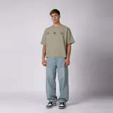 Remera boxy de color crudo con hombro caído y corte cuadrado a la cadera. En el frente presenta un diseño minimalista con texto y un pequeño logo central.