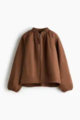 Campera bomber oversized color marrón con cuello elevado fruncido, cierre frontal y mangas raglán con puños elásticos.