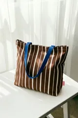 Tote bag de tela a rayas marrones y blancas con asas de hombro en color azul.