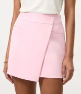 Short pollera de sastrería color rosado, con diseño asimétrico superpuesto en el frente, bolsillos ribeteados decorativos y cierre lateral discreto.