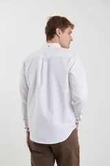 Camisa de vestir blanca de manga larga, con cuello abotonado, bolsillo frontal y botones en tono madera.