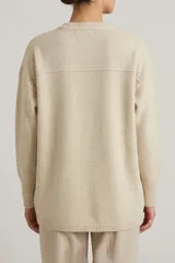 Buzo de punto color beige, con cuello redondo, mangas largas y diseño con aberturas laterales en el ruedo.