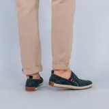 Alpargata de gamuza color verde oscuro, con detalle de elástico lateral a rayas rojas y blancas. Presenta una suela con borde de yute trenzado y base de goma.