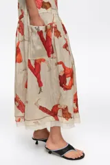 Vestido midi con vuelo en el bajo, de corte recto con tirantes anchos y escote cuadrado, confeccionado en mezcla de lyocell. Presenta un estampado artístico integral con figuras humanas en tonos rojos y naranjas sobre fondo crudo, además de costuras visibles decorativas.