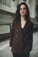 Blazer de corte sastre con cuello solapa, manga larga y hombreras marcadas. Presenta un diseño cruzado con cierre frontal de botones, bolsillos delanteros de vivo y abertura posterior en el bajo.
