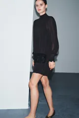 Vestido corto de viscosa color negro con cuello perkins y manga larga. Presenta un fajín de terciopelo integrado con bordados a tono y detalle de lazadas laterales.