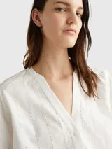 Blusa blanca de algodón orgánico con cuello en V, mangas largas abullonadas con puños abotonados y detalles de encaje vertical.