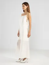 Vestido largo de color celeste confeccionado en tejido arrugado liviano. Presenta un diseño con escote recto, breteles finos y detalles de lazos en los laterales. Incluye bolsillos laterales, forro interno corto y un ruedo asimétrico con caída posterior más larga.