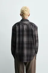 Camisa de corte relajado confeccionada en tejido fluido con mezcla de viscosa. Presenta diseño de cuadros en tonos grises y azul oscuro, cuello solapa, manga larga con puños abotonados y cierre frontal de botones.