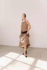Vestido largo color marrón de crepé plissé, con escote halter adornado con detalles de perlas, silueta fluida y lazo ajustable en la cintura.