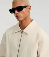 Campera masculina de corte boxy en color beige, con cuello inglés, cierre frontal de cremallera, mangas largas con puños elásticos y ruedo con elástico. Presenta bolsillos laterales y detalles de recortes en el diseño.