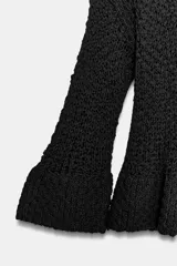 Jersey de punto color negro con cuello redondo y mangas largas terminadas en volantes acampanados.