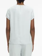 Blusa celeste de poliéster reciclado con cuello redondo, mangas cortas y cierre con cremallera en la espalda. Presenta una abertura en la parte delantera con una barra metálica decorativa.