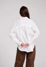 Camisa blanca de corte holgado con cuello camisero y cierre frontal de botones. Presenta un delicado bordado vertical de flores pequeñas en color bordó a lo largo de la botonera y en el cuello.