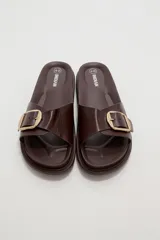 Sandalia plana de eco cuero negro, con tira ancha en el empeine decorada con una hebilla metálica dorada cuadrada y suela dentada.