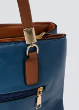 Cartera azul de cuero sintético con doble asa corta color marrón. Tiene dos compartimentos principales con cierre y bolsillos internos. Incluye correa larga extraíble.