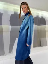 Tapado largo de fieltro de lana merino con teñido artesanal tie-dye en degradé de azul. Tiene cuello alto, cierre lateral con broches ocultos, bolsillos laterales y corte amplio.