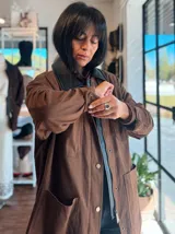 Campera de ecocuero color chocolate, con corte amplio y relajado. Presenta cuello camisero, cierre frontal con botones metálicos y bolsillos frontales de gran tamaño.