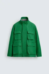 Chaqueta tipo cazadora de corte relajado en color verde, confeccionada en tejido de mezcla de algodón. Presenta cuello subido con forro interior a cuadros, manga larga con puños abotonados y cuatro bolsillos frontales de plastrón con solapa. Incluye cierre frontal de cremallera oculta por solapa con botones a presión y cintura ajustable en el interior.