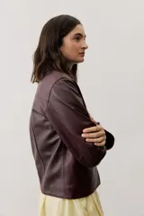 Chaqueta de cuero negra con cuello redondo, cierre frontal de botones forrados y bolsillos ribeteados con detalles de costura decorativa.