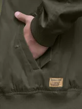 Campera tipo bomber color marrón, confeccionada en tela encerada, con cierre frontal, cuello tipo mao y puños y ruedo acanalados.