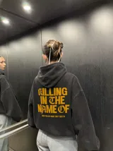 Hoodie canguro con cierre frontal, color negro con efecto acid wash, con capucha y bolsillos tipo canguro. Presenta el texto estampado en amarillo "Now You Do What They Told Ya" en el pecho.