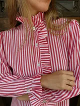 Camisa de manga larga con estampado de rayas verticales en color rojo y blanco. Presenta cuello alto con volados, cierre frontal con botones y detalles de volados en la solapa y en los puños.