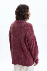 Buzo de punto chenille en color bordó, con cuello redondo, mangas largas y aberturas laterales en el ruedo. Presenta un diseño de textura acanalada en el cuello, hombros y puños.