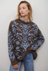 Buzo de tejido de punto en color marrón con un patrón ornamental floral en color celeste. Presenta cuello redondo, mangas largas y un corte holgado.