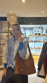 Cartera de gamuza marrón marca Chérie, de diseño clásico y amplio, con costuras visibles, una costura central vertical y asa ajustable.