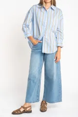 Camisa de corte oversize con estampado de rayas verticales en tonos azul y beige. Presenta cuello camisero clásico, cierre frontal con botones, bolsillo en el pecho y mangas largas con puños rectos.