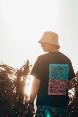 Remera negra de corte amplio con estampado en la espalda con un diseño rectangular con texto y una ola en colores celeste, rosa y blanco.