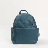 Mochila de cuero sintético con textura granulada en color turquesa. Presenta un compartimento principal con cierre, un bolsillo frontal con cierre y bolsillos laterales abiertos. Incluye asa superior y correas ajustables.