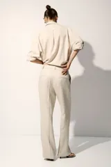 Pantalón sastrero color beige de tiro alto, confeccionado en mezcla de lino y lyocell. Presenta diseño de perneras rectas con pliegues frontales y traseros, bolsillos al bies y trabillas para cinturón.