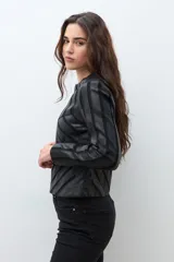 Chaqueta negra de eco cuero con cierre frontal y cuello redondo. Presenta paneles con diseño geométrico de tiras en relieve en el frente y mangas.