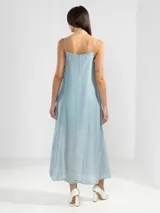Vestido largo de color celeste confeccionado en tejido arrugado liviano. Presenta un diseño con escote recto, breteles finos y detalles de lazos en los laterales. Incluye bolsillos laterales, forro interno corto y un ruedo asimétrico con caída posterior más larga.
