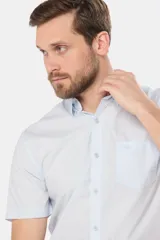 Camisa lisa de manga corta color celeste, confeccionada en algodón, con cuello abotonado y bolsillo en el pecho con logo bordado.